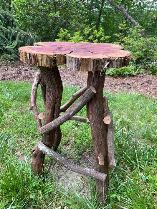 The side table pictured features a base made of rustic mountain laurel branches and a tabletop made from a cedar slab with a food-safe finish. 